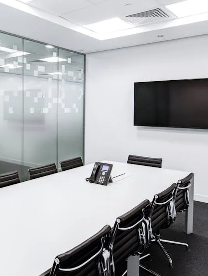 A conference room with big white table, black chairs and hanging monitor.