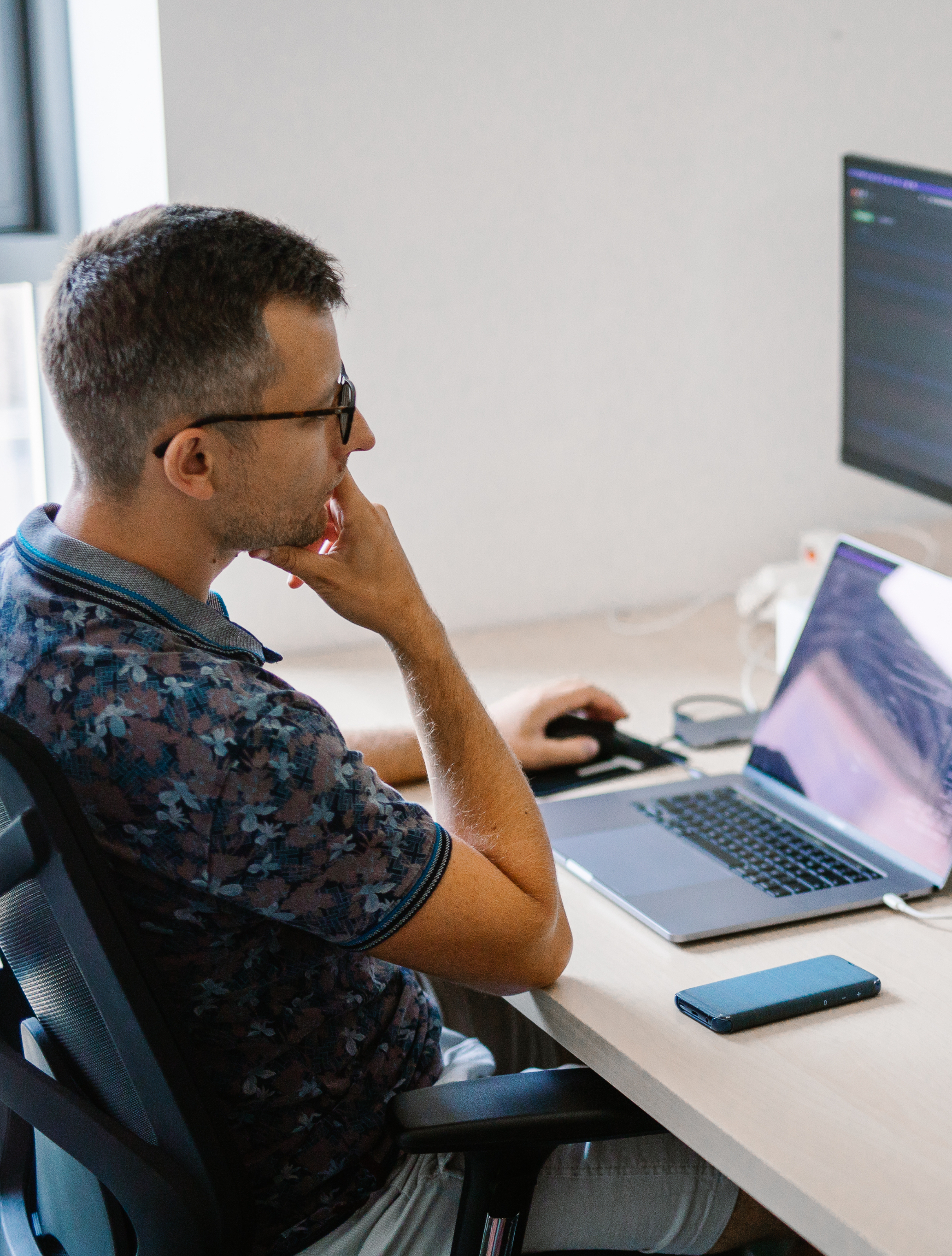 Man wearing glasses sitting at a desk in an office, focused on working on his laptop.