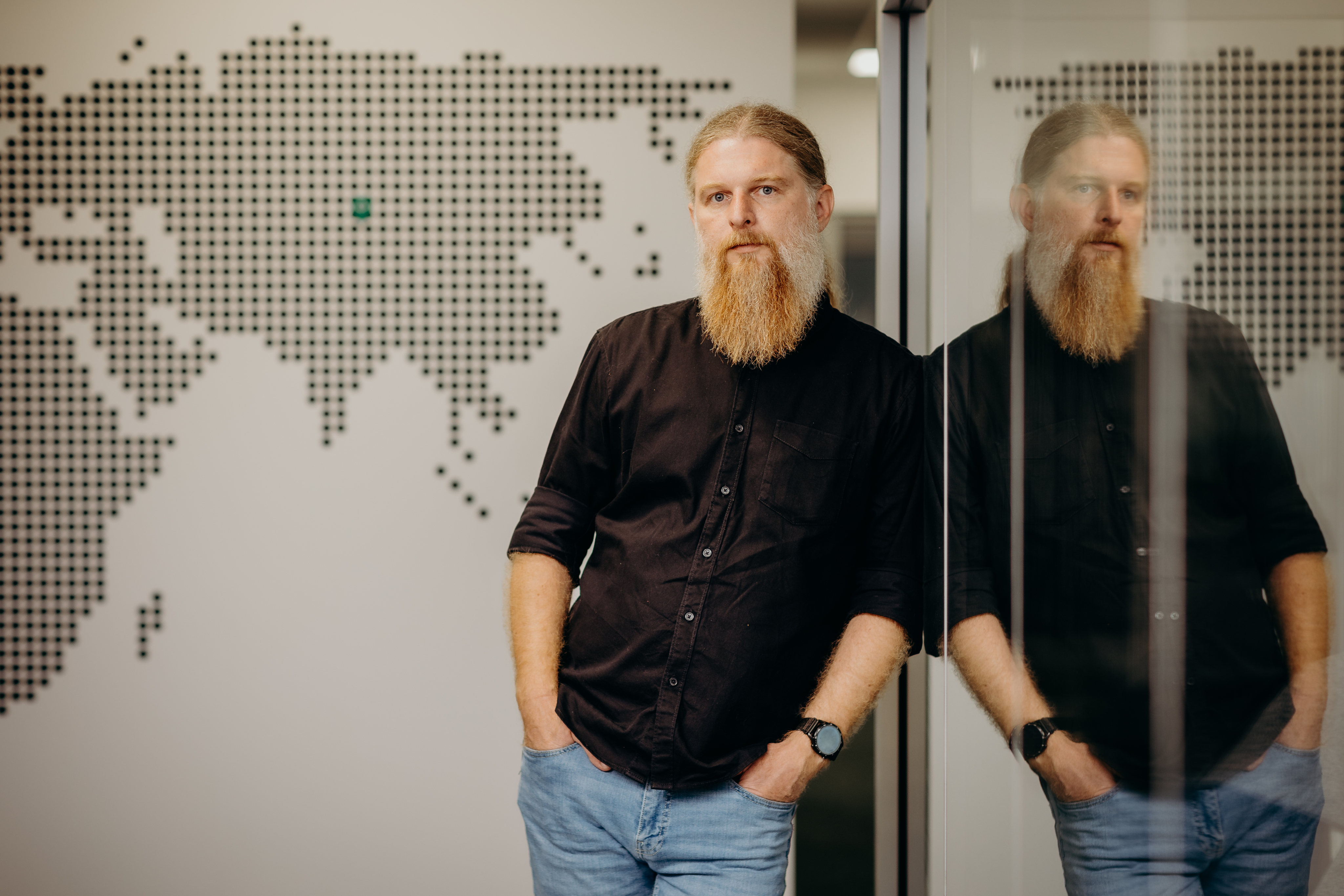 Man leaning against a glass wall in an office with a world map graphic in the background