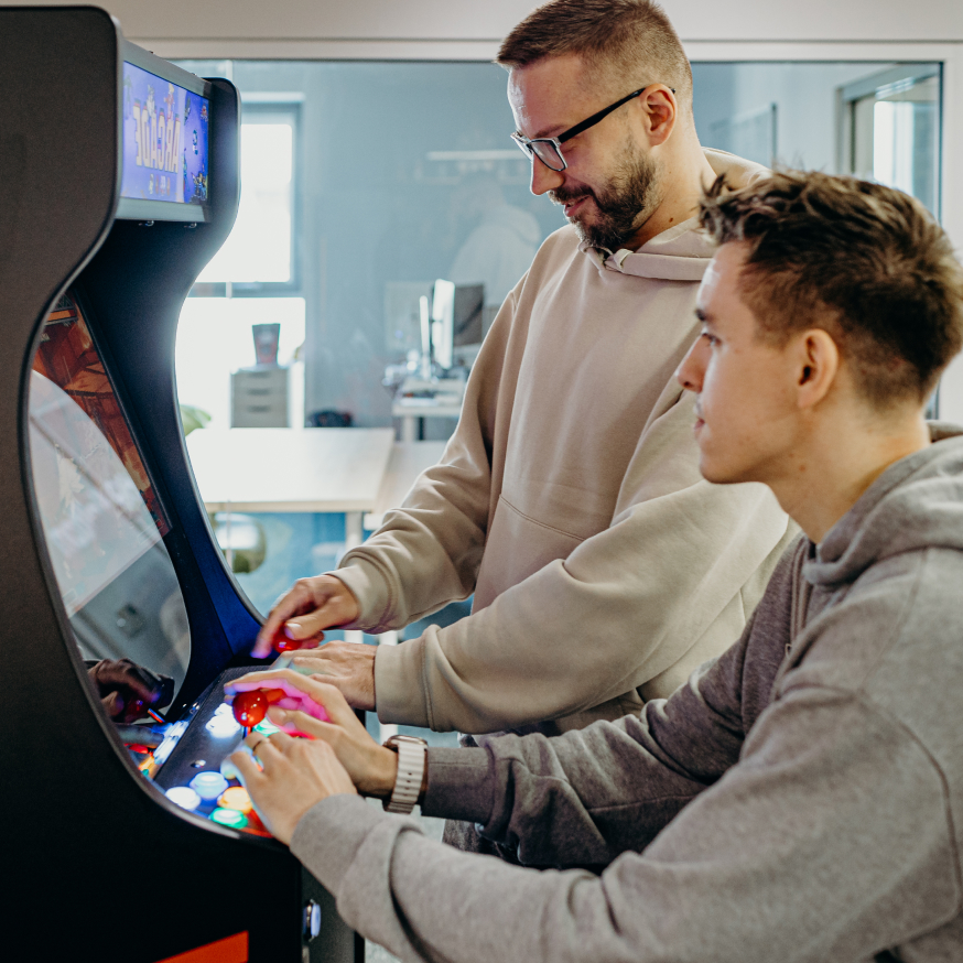 Two coworkers playing on an arcade machine in a casual office environment